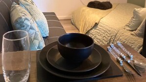 Een kamer met een bed, een televisie waarop 'NETFLIX' staat, een tafel met een kom, een glas en bestek.