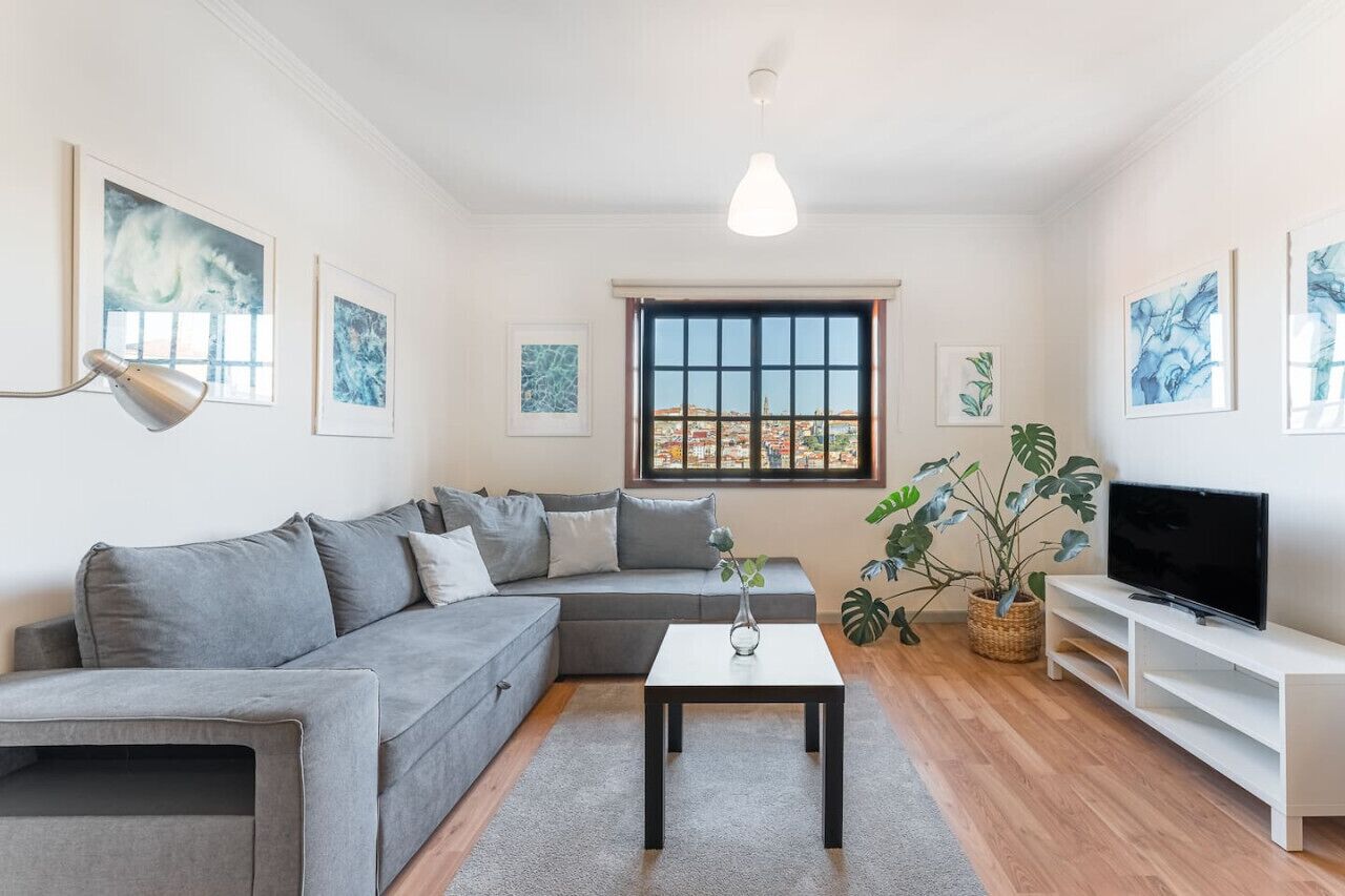 A modern living room with a grey sofa, a coffee table, a TV on a white stand, and artwork on the walls.