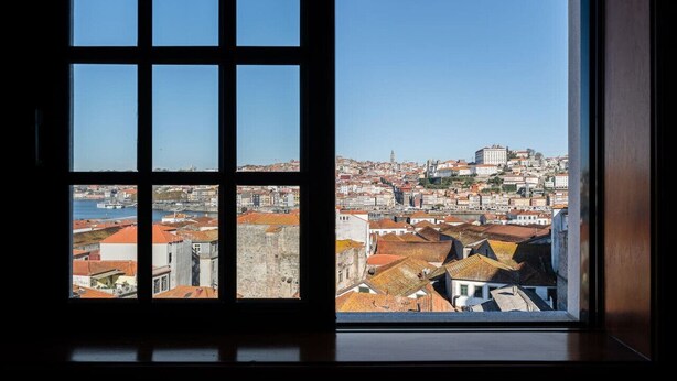 A view from a window with a grid of panes, overlooking a cityscape with historic buildings and a prominent tower. - Dream Views of Porto - Private Apt in Gaia by Lisbeyond (Vila Nova de Gaia)