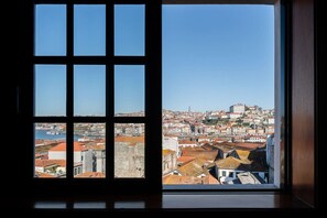 Une vue depuis une fenêtre à carreaux, donnant sur un paysage urbain avec des bâtiments historiques et une tour imposante.