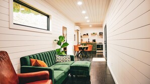 A modern living room with a green sofa, a brown leather armchair, and a dining area with orange chairs. - Unique Cabin on the Beechfork River, nestled in the heart of the Bourbon Trail  (Springfield)