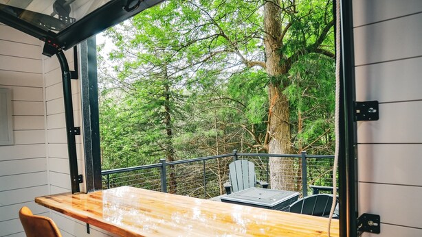 A wooden table with chairs in a room with a view of a forest. - Unique Cabin on the Beechfork River, nestled in the heart of the Bourbon Trail  (Springfield)
