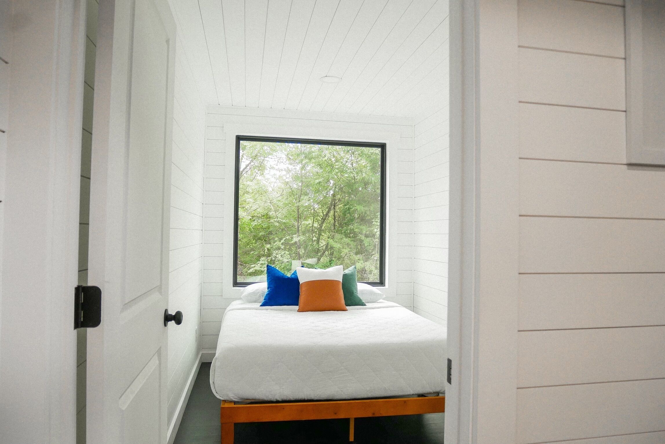 Una habitación pequeña con una cama, un ventanal y una puerta.