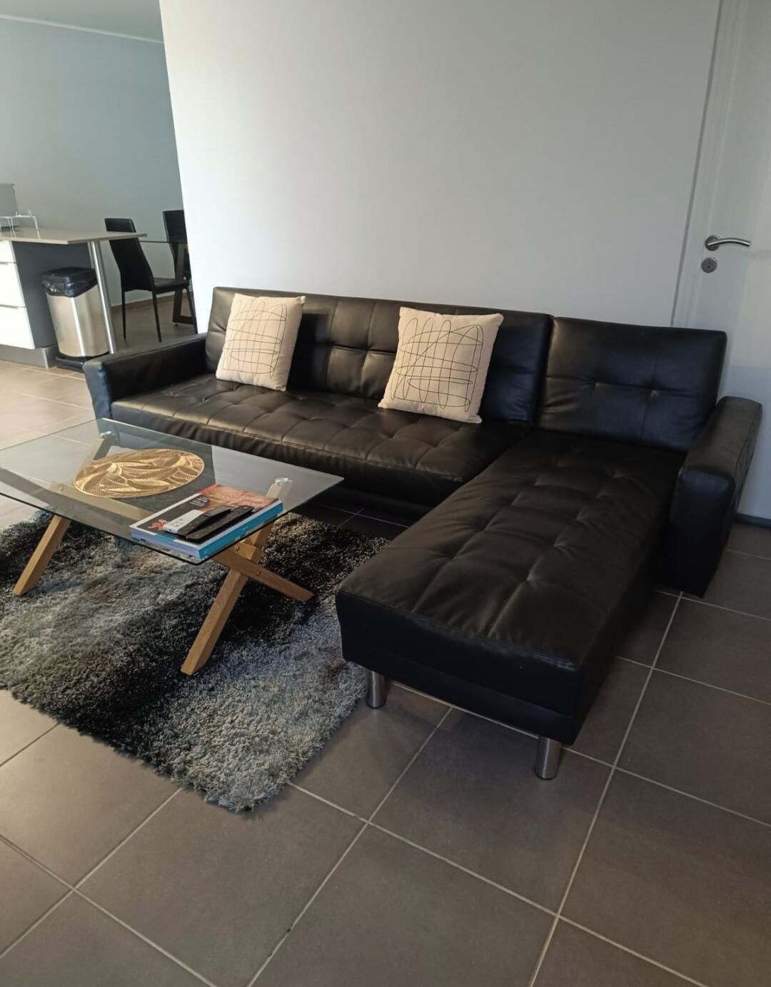 Un salon moderne avec un canapé en cuir noir, une table basse en verre et un tapis noir à longues mèches.