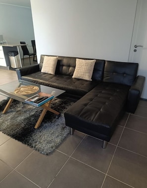 A modern living room with a black leather sofa, a glass coffee table, and a black shag rug.