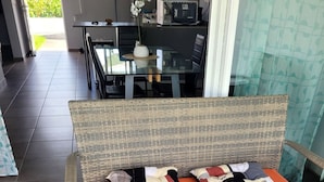 Una silla de mimbre con cojines naranjas y una mesa de vidrio con un florero y un cuenco.
