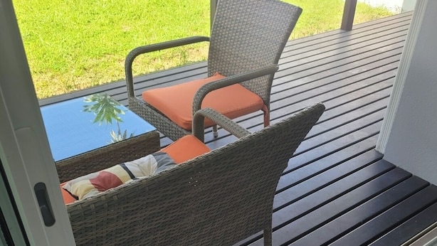 Un área de estar al aire libre techada, con mobiliario de mimbre y una mesa de vidrio.
