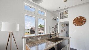A modern kitchen with a granite countertop, a built-in dishwasher, and a large window overlooking a backyard. - Site 93 @ Peninsula point (Kerens)