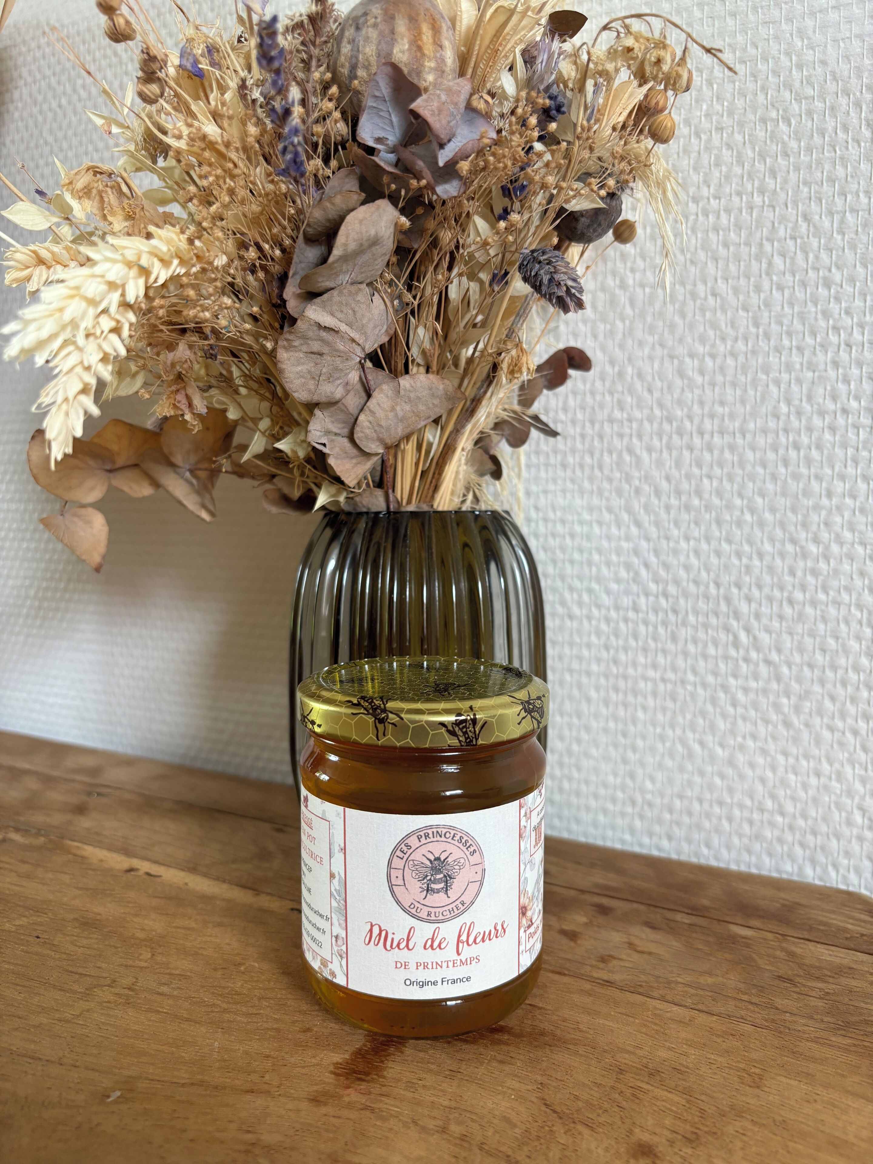 A jar of Miel de fleurs de printemps on a wooden surface.