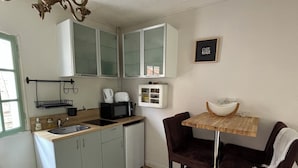 Une cuisine compacte équipée d’un évier, d’un four à micro-ondes et de placards. On y trouve une table en bois avec des chaises et un lustre.