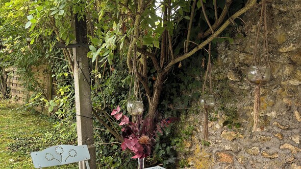 Un espace de restauration en plein air avec une table dressée pour deux personnes, entouré de verdure et bordé d’un mur en pierre.