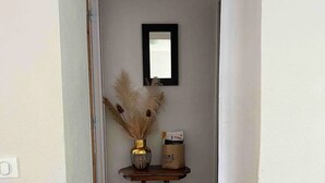 Un couloir doté d’un plancher en bois, une petite table sur laquelle est posé un vase contenant des herbes des pampas séchées, et un miroir encadré accroché au mur.