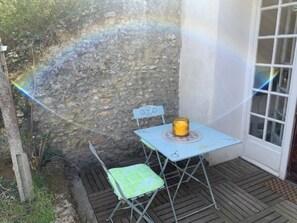 A small outdoor seating area with a table and chair, a stone wall, and a door. - Maisonnette à la Campagne (Baulne)