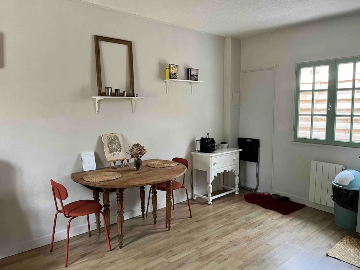 Un coin repas avec une table en bois, des chaises rouges, un meuble blanc et une fenêtre avec des stores.