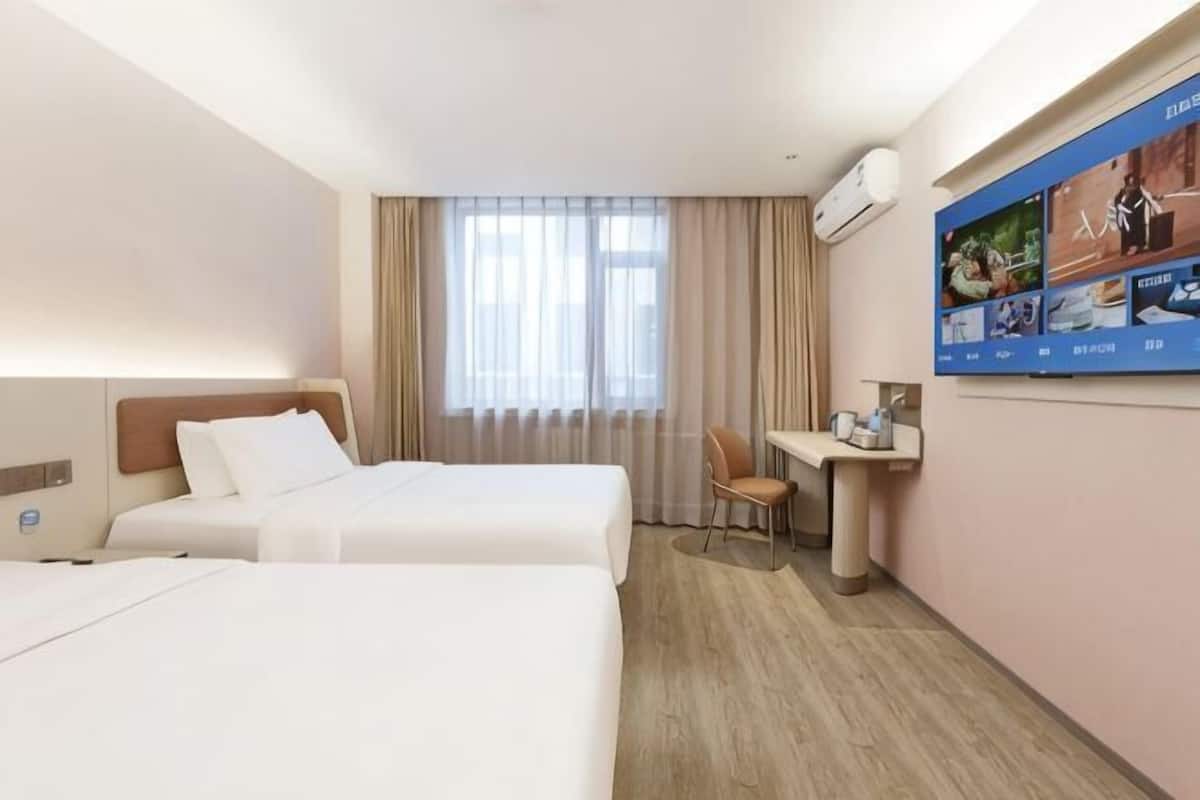 A hotel room with two beds, a desk, a chair, and a large window with curtains.