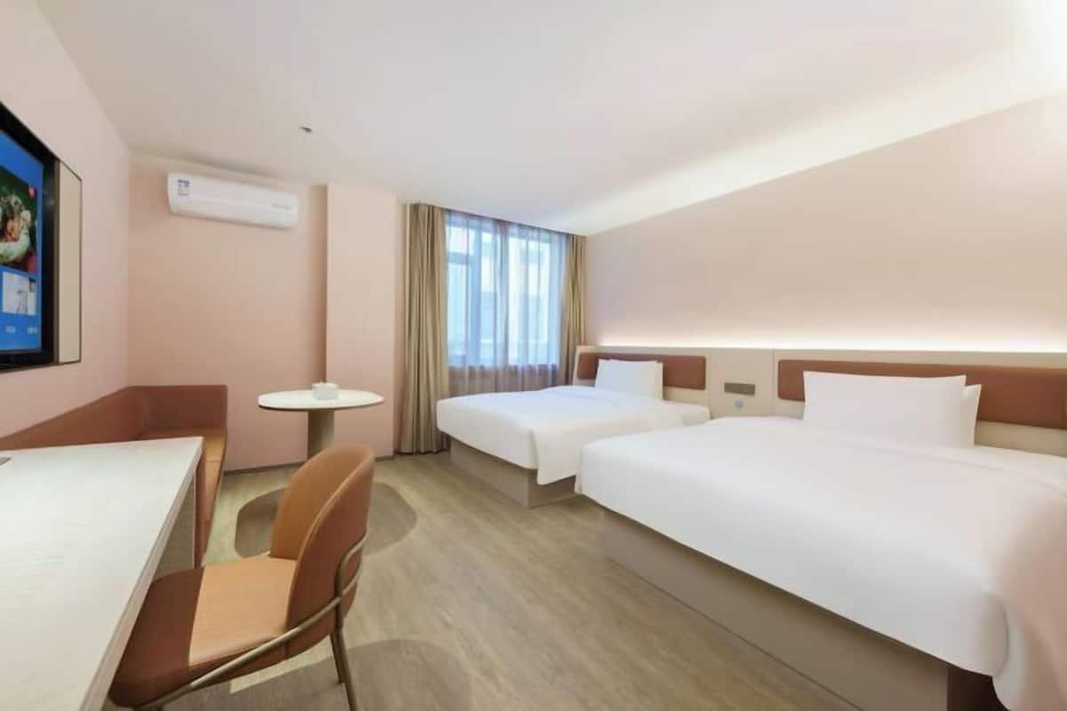 A hotel room with two beds, a desk, a chair, a small table, and a window with curtains.