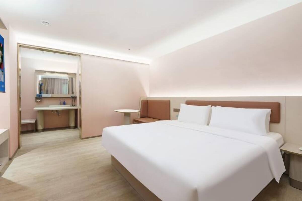 A hotel room with a large bed, a bedside table, a small round table, and a bathroom with a sink and mirror.