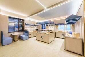 A modern interior with seating areas, a counter with food display, and a view through large windows. - HanTing Hotel (Dalian Zhongshan Square Subway Station) (Dalian)