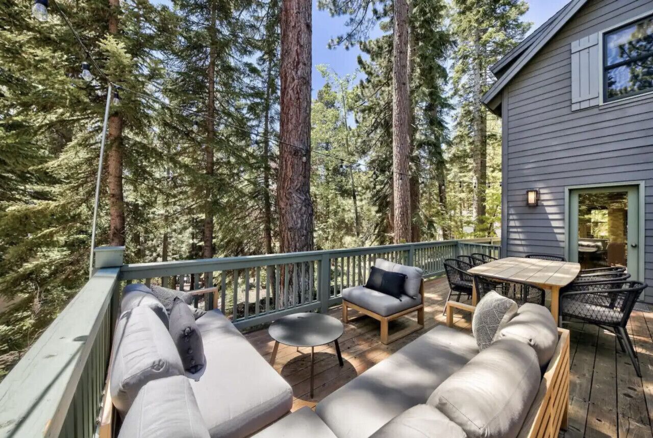 A deck with a sofa, chairs, and a table, surrounded by tall trees.