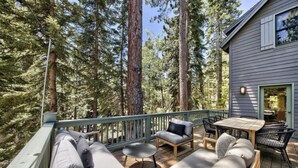 Une terrasse avec un canapé, des chaises et une table, entourée de grands arbres.