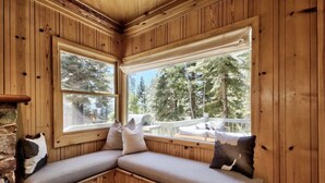 L’intérieur d’un chalet en bois, avec un banc intégré et de grandes fenêtres donnant sur une terrasse et des arbres.