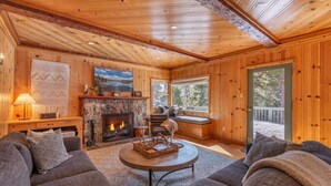 L’intérieur chaleureux d’un chalet en bois, avec une cheminée, des sièges confortables et de grandes fenêtres offrant une vue sur l’extérieur.
