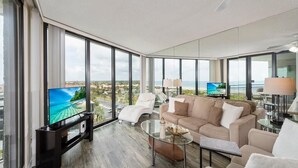 A modern living room with a large TV, comfortable seating, and a view of the ocean. - Stunning Ocean Views: Seventh-Floor Beach Condo! (Saint Augustine)