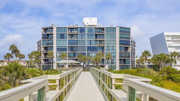 A modern hotel with a multi-story structure, a wooden boardwalk leading to the entrance, and a clear view of the surrounding greenery. - Stunning Ocean Views: Seventh-Floor Beach Condo! (Saint Augustine)