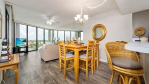 A modern dining area with a wooden table and chairs, a chandelier, and a large window offering a view of the outdoors. - Stunning Ocean Views: Seventh-Floor Beach Condo! (Saint Augustine)