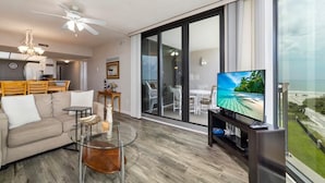 A modern living room with a sofa, glass coffee table, and a TV. - Stunning Ocean Views: Seventh-Floor Beach Condo! (Saint Augustine)