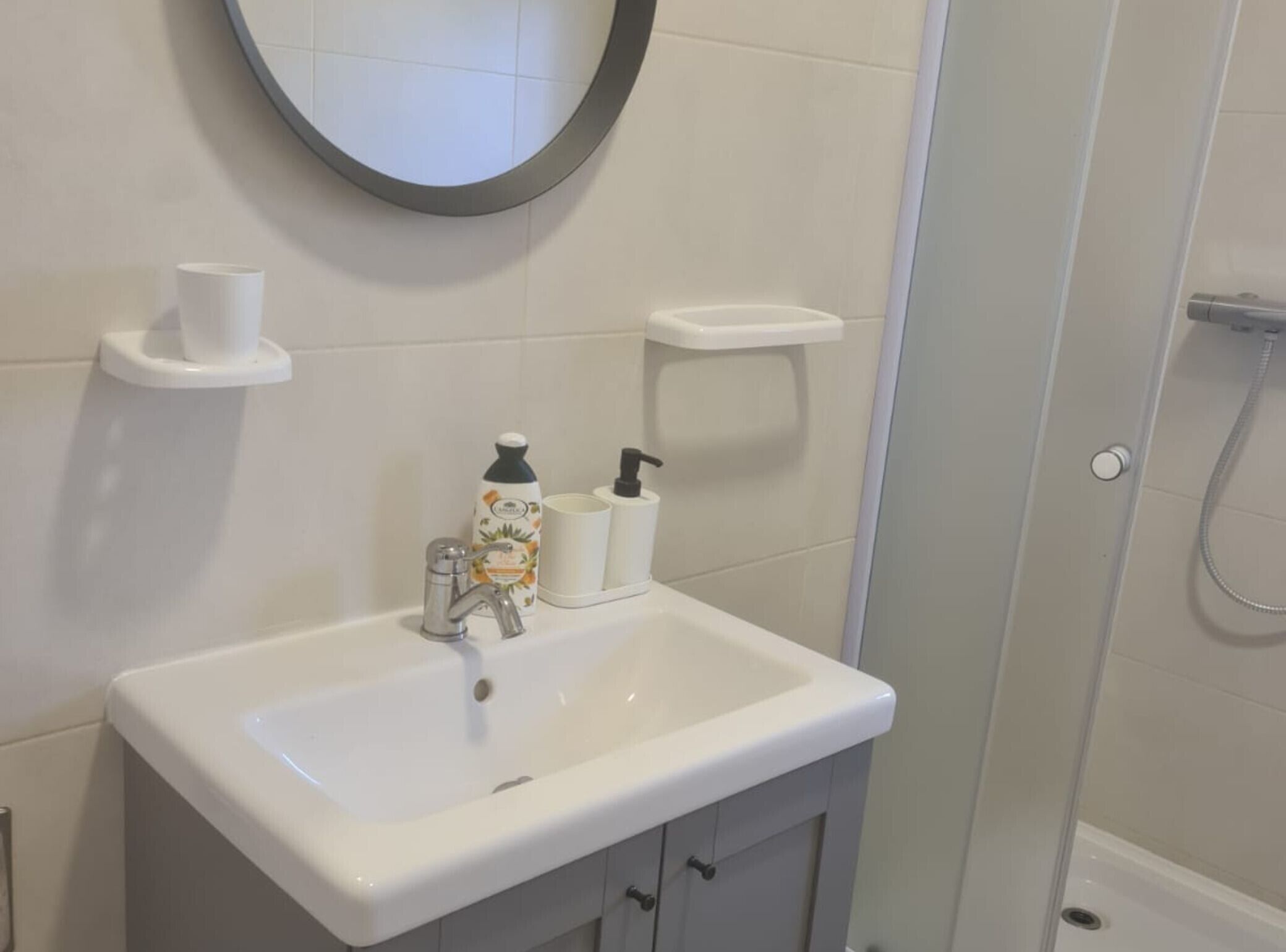 A bathroom with a white sink, a mirror, a toilet paper holder, and a shower area.