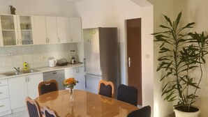 Een compacte keuken met witte kastjes, een eettafel met stoelen en een potplant.