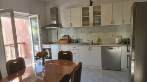 Een moderne keuken met witte kastjes, een RVS vaatwasser en een eethoek met een houten tafel en stoelen.