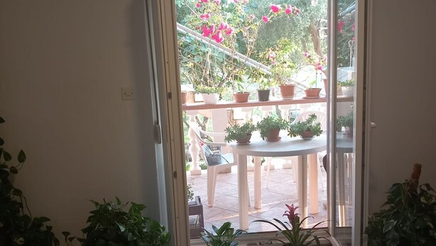 Een kamer met een schuifglasdeur die uitkomt op een buitenruimte met potplanten en een tafel.