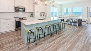 A modern kitchen with white cabinets, stainless steel appliances, and a large island with bar stools. - Beachfront House with Pool! 6 BR/6.5 Beachfront Paradise! (Gulf Shores)