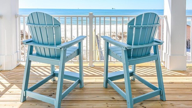 Two light blue Adirondack chairs facing a wooden deck with a white railing, overlooking a beach with the ocean in the background. - Beachfront House with Pool! 6 BR/6.5 Beachfront Paradise! (Gulf Shores)