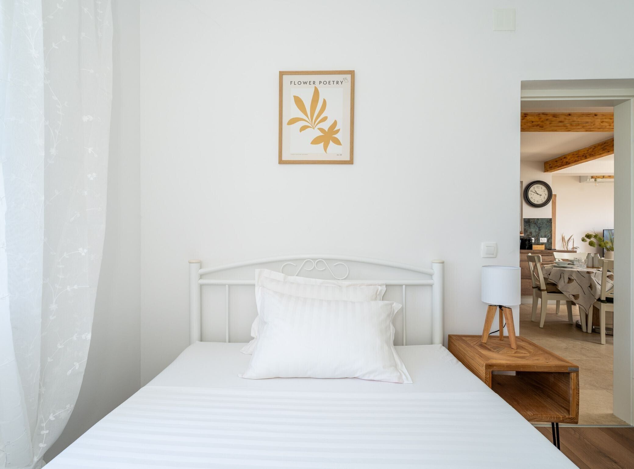 Een slaapkamer met een wit bed, een houten nachtkastje met een lamp en een lijst met een foto aan de muur.