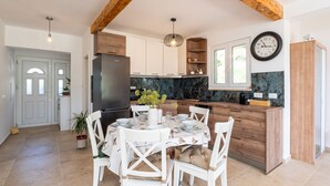 A modern kitchen with a large island, wooden beams, and a dining area with white chairs and a table set for four.