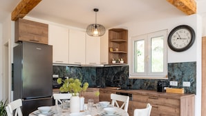 A modern kitchen with wooden cabinets, a stainless steel refrigerator, and a dining area set for four with white chairs and a table set with plates and glasses.