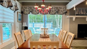 A dining room with a large wooden table, six chairs, a chandelier, and a view of the outdoors through large windows. - Walk to Beach, Stunning Sunsets (Southampton)