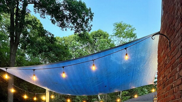 An outdoor patio with wicker furniture, a blue canopy, and string lights. - Walk to Beach, Stunning Sunsets (Southampton)
