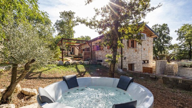 Una casa de piedra con un jacuzzi en primer plano y una pérgola al fondo.