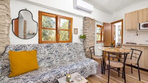 Un espacio de estar acogedor con un sofá estampado, una mesita con una vela y una mesa de comedor con sillas. Se observa una zona de cocina con armarios de madera y un microondas.