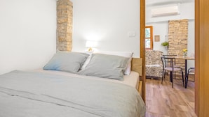 Un dormitorio con una cama, una pared de piedra, un escritorio con silla y una mesita con un jarrón.