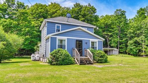 A two-story house with a front porch, a satellite dish, and a small shed in a grassy yard surrounded by trees. - Charming Catskills Getaway: Hike, Bike, Sip & More (Acra)