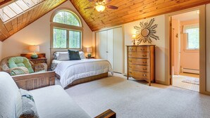 Une chambre avec un plafond en pente, une grande fenêtre, un lit, une commode et une chaise.