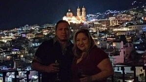 Two people standing on a balcony overlooking a cityscape at night with illuminated buildings and a prominent church in the background. - Hotel Taxco De Mis Amores (Taxco)