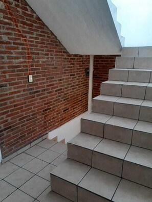 Una escalera con un muro de ladrillo a un lado y un muro de concreto al otro, que conduce a un nivel superior.