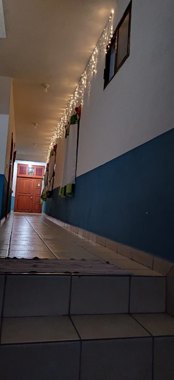 Un pasillo con suelo de baldosas, una puerta de madera al final y luces colgantes en el techo.