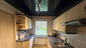 A modern kitchen with light wood cabinets, a black countertop, and a window with a view of greenery. - Ferienhaus in Herzwolde für 4+2 Personen (Wokuhl-Dabelow)